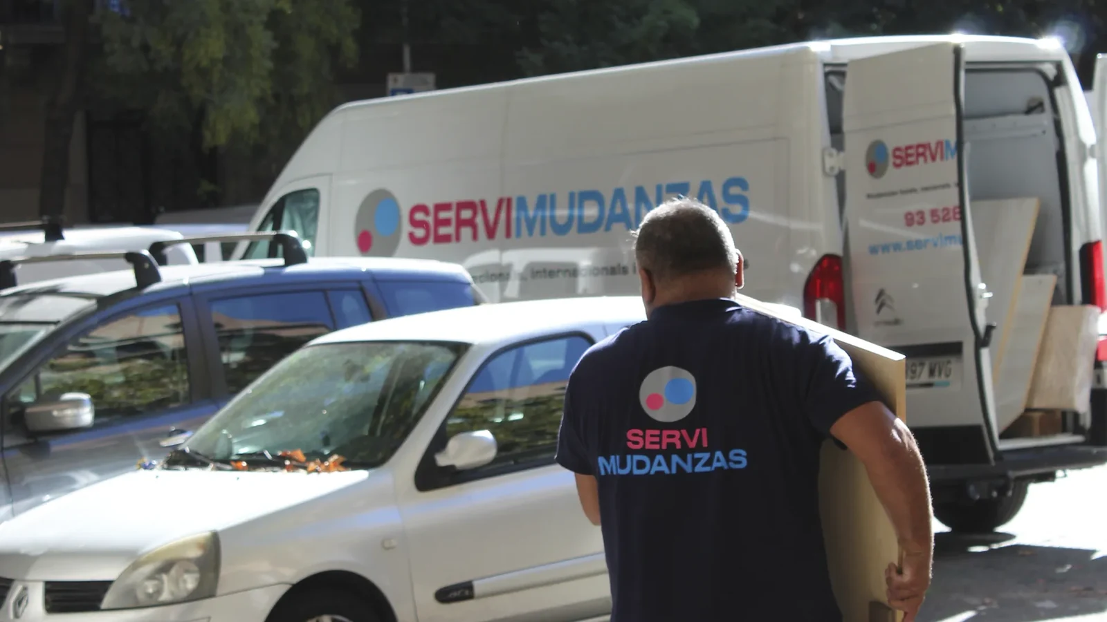 Operario de Servimudanzas con caja de cartón junto a furgoneta de mudanza en calle de Barcelona